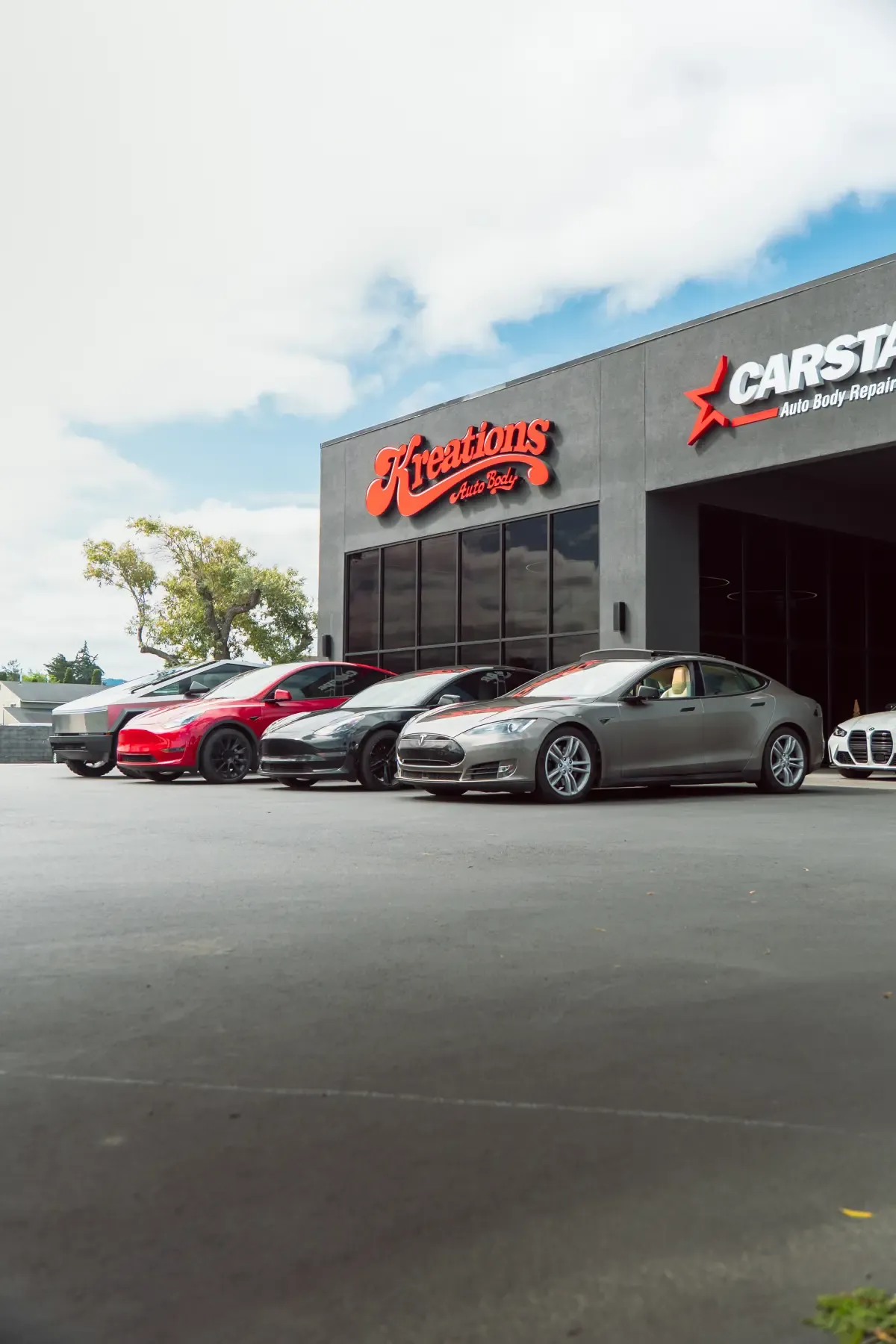 A lineup of Teslas parked in front of the Kreations Auto Body and CARSTAR sign in Fortuna
