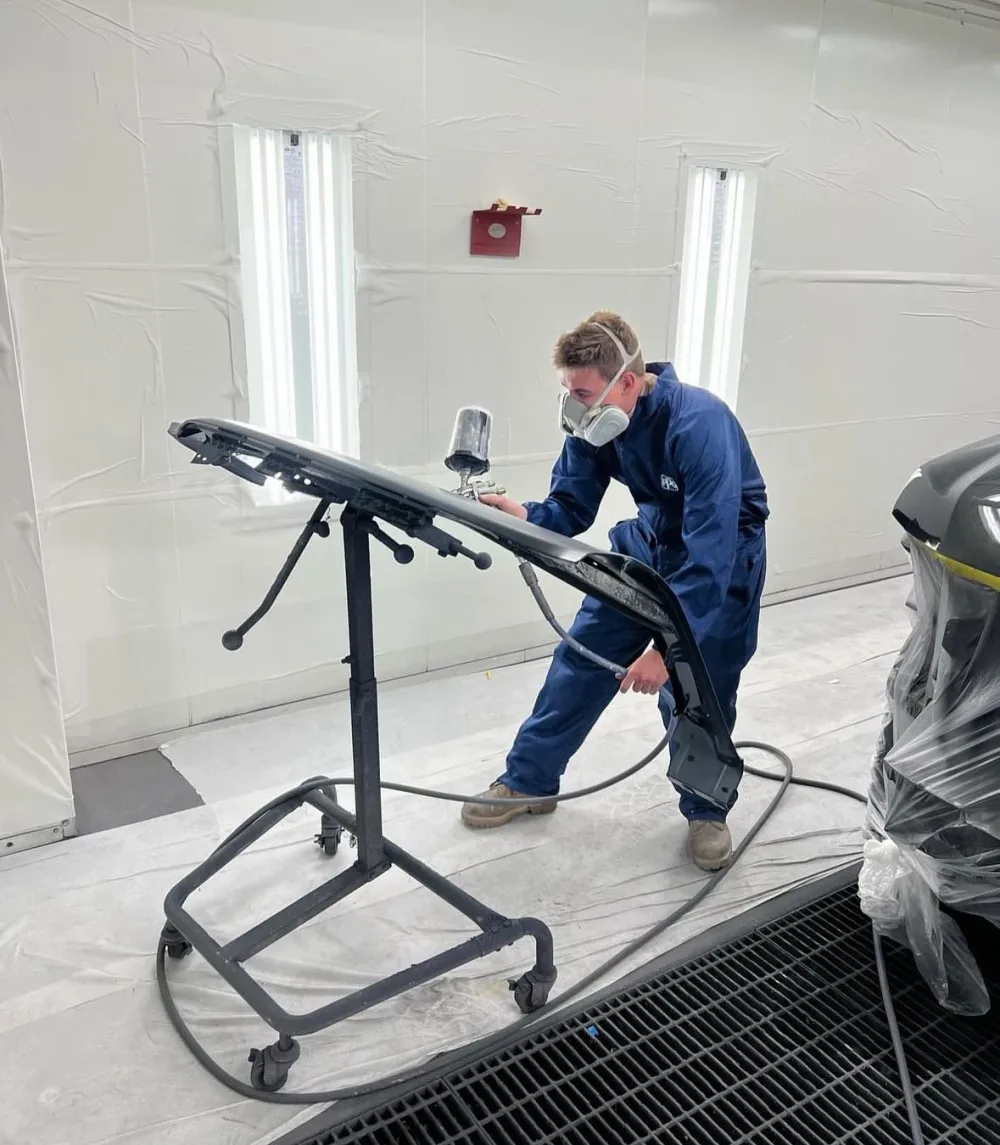 Kreations Auto Body technician refinishing a bumper panel in the spray booth