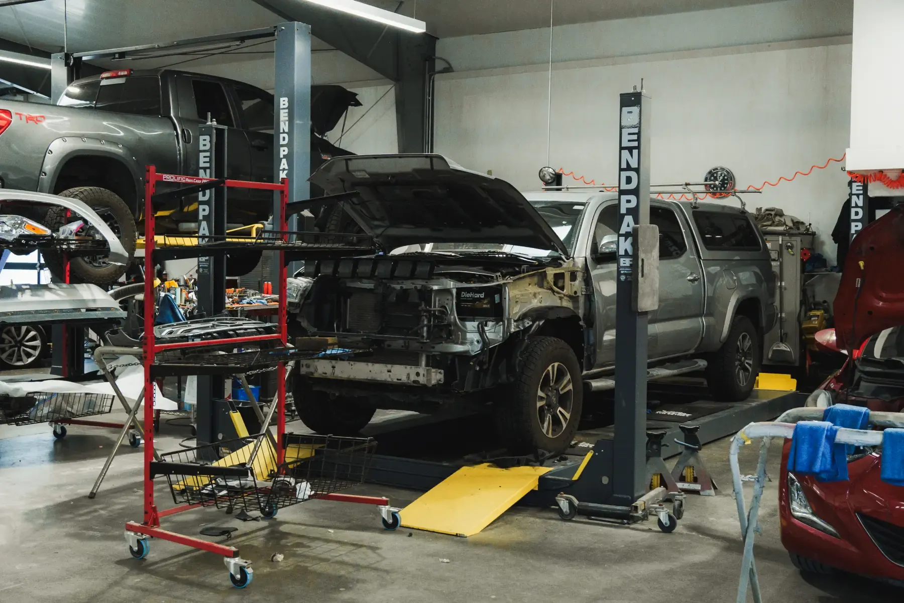 Truck up on a lift with its front end stripped for collision repair inside the Kreations Auto Body shop in Fortuna